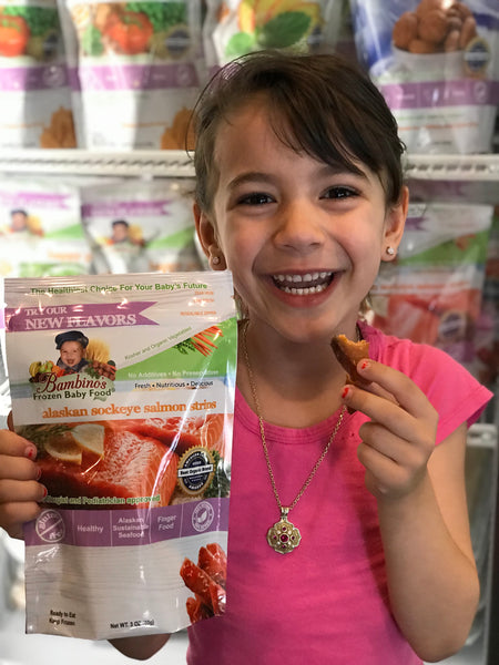 Alaskan Sockeye Salmon Strip for teething baby toddler snack finger food omega rich best product Bambinos baby food Zoi Maroudas healthy food product natural non gmo home delivery family business smiling cute girl boy eating fish 